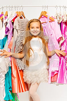 Small cute girl standing between hangers in shop