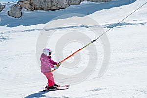 Small cute girl taking a ski lift and learning to ski on a sunny day.