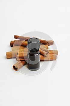 Small dark glass bottle in front of cinnamon sticks on white. Essential oil or extract. Cosmetic or food concept