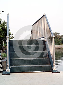 Small dark green diamond metal plate bridge staircase with gray steel railings on canal side concrete pathway