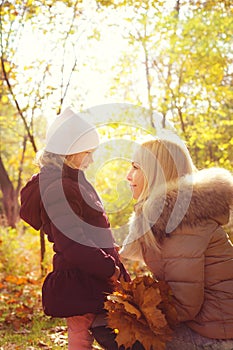 Small daughter and her mother looking at each other and smiling, happy childhood, backlight in autumn park.