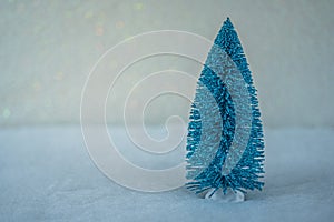 Small decorative blue Christmas tree with artificial snow on light blue background