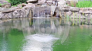 A small decorative waterfall splashes into the pond. Landscaping using stone and water in a park or garden. Natural landscape in