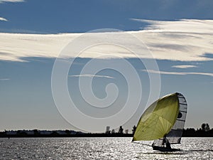 A small dinghy with large yellow sail under a blue sky sailing on a lake