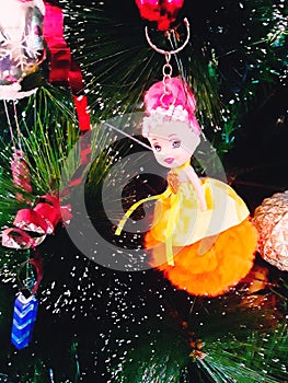 A small doll in an orange dress in New Year's entourage. Spruce branch's New Year, festive decorations.