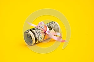 Small dollar gift, Bundle of bills of one hundred dollars tied with a pink ribbon. Dollars isolated on yellow background