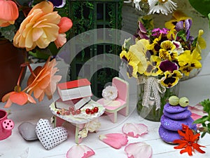 Small dollhouse chair, table with tiny books among beautiful flowers of daisy and begonia. Fairies in the garden