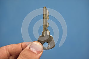 Small door key in hand on a blue background