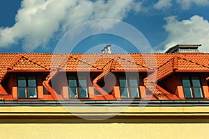 Small dormer windows in a red tiled roof against blue sky background