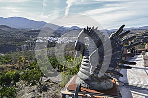 Small dragon sculpture on top of a fence decorating a viewpoint with a town in the background photo