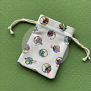 A small drawstring pouch on a green textured surface. The pouch is made of white