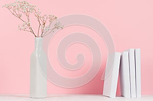 Small dried flowers in elegant vase and white books on wood table and soft pastel pink background, copy space.