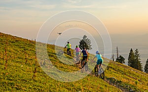 Small drone flies along a group of tourists mountain biking on a sunny evening.