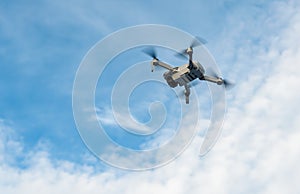 Small drone flying in a cloudy blue sky.