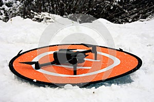 A small drone on its landing base among the cold white snow in the mountains in winter