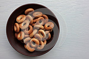Small dry bagels for kids in brown ceramic bowl on white wooden background. Healthy snack