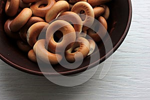 Small dry bagels for kids in brown ceramic bowl on white wooden background. Healthy snack
