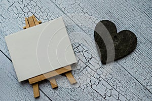 Small easel with a blank canvas over white and dark wooden heart. Old wooden background and big copy space for your sign