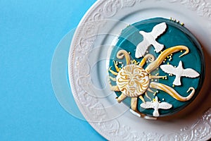 Small easter blue cake with yellow sun and white doves in the white plate. Blue background.