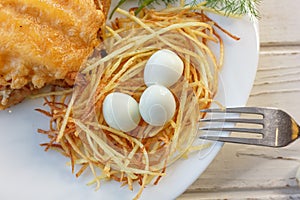 Small eggs in a nest made with potatoes on a white plate