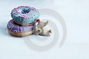 A small elephant figurine propped up with two different colored donuts,