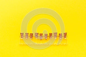 Small empty transparent bottles with stoppers laid out in a row on a yellow background