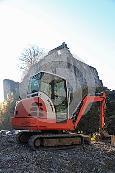 Small excavator on a consruction site hill in front of an ancient castle ruin