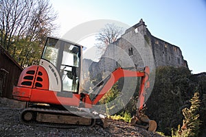 Small excavator on a consruction site hill in front of an ancient castle ruin