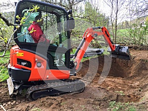 Small excavator with man inside, at work making garden pond