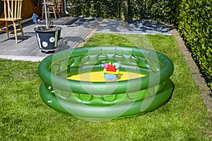 A small family pool for children in green color, placed on the grass in the garden.