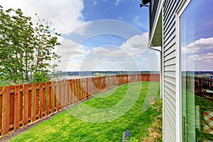 Small fenced backyard of a large blue house. With grass filled garden.