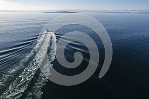 Small ferry boat in blue ocean on the way to Aran island, Ireland. Wake behind cruise ship. Warm sunny day with clear blue sky.