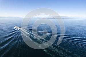 Small ferry boat in blue ocean on the way to Aran island, Ireland. Wake behind cruise ship. Warm sunny day with clear blue sky.