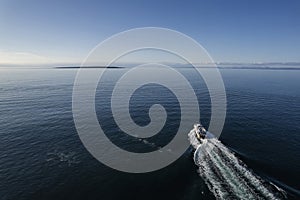 Small ferry boat in blue ocean on the way to Aran island, Ireland. Wake behind cruise ship. Warm sunny day with clear blue sky.