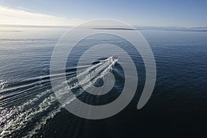 Small ferry boat in blue ocean on the way to Aran island, Ireland. Wake behind cruise ship. Warm sunny day with clear blue sky.