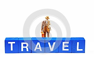 A small figurine holding a suitcase behind the word `travel`