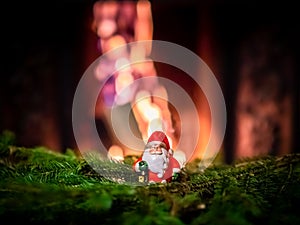 A small figurine of Santa Claus stands on green spruce branches against the background of flames in the fireplace