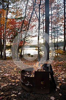 Small fire pit on a campsite by the lake in Fall with colourful foliage