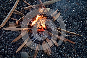 Small fire of split cedar on a pebble beach in the evening.