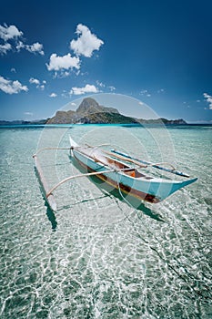 Small fishing banca boat in front of Cadlao Island in crystal clear shallow water, low tide, amazing nature of Palawan