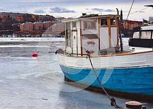 Fishing boat with a blue hull moored on a frozen river in winter
