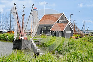 A small fishing boat at the jetty next to a black Dutch house in green grass