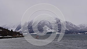 Small fishing boat on Lyngen fjord near Skibotn, Troms og Finnmark, Norway chased by a swarm of seagulls in winter.