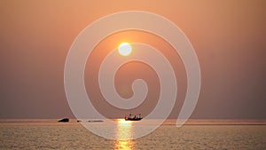 A small fishing boat moored in the middle of the sea during sunset in Thailand