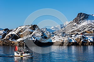 Small fishing boat near Svolvaer on the Lofoten islands in Norway with snow on clear day with blue sky