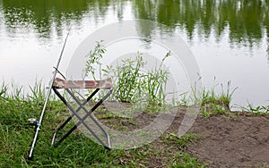 A small fishing chair for one person with a military print stands on the grass next to the lake. Fishing concept.