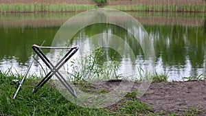 A small fishing chair for one person stands on the grass next to the lake. Fishing concept.