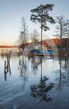 Small fishing wooden house with a pier and boats on the shore of the north lake in on a sunny day. First frost