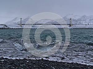 Small floating iceberg with clear surface floating on Diamond Beach near JÃ¶kulsÃ¡rlÃ³n, Iceland in winter with bridge.