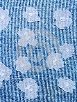 Small flowers cutted of fine white fabric, sewn randomly on blue denim.